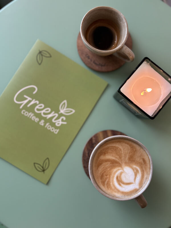 Zelené desky s logem Greens, káva a svíčka