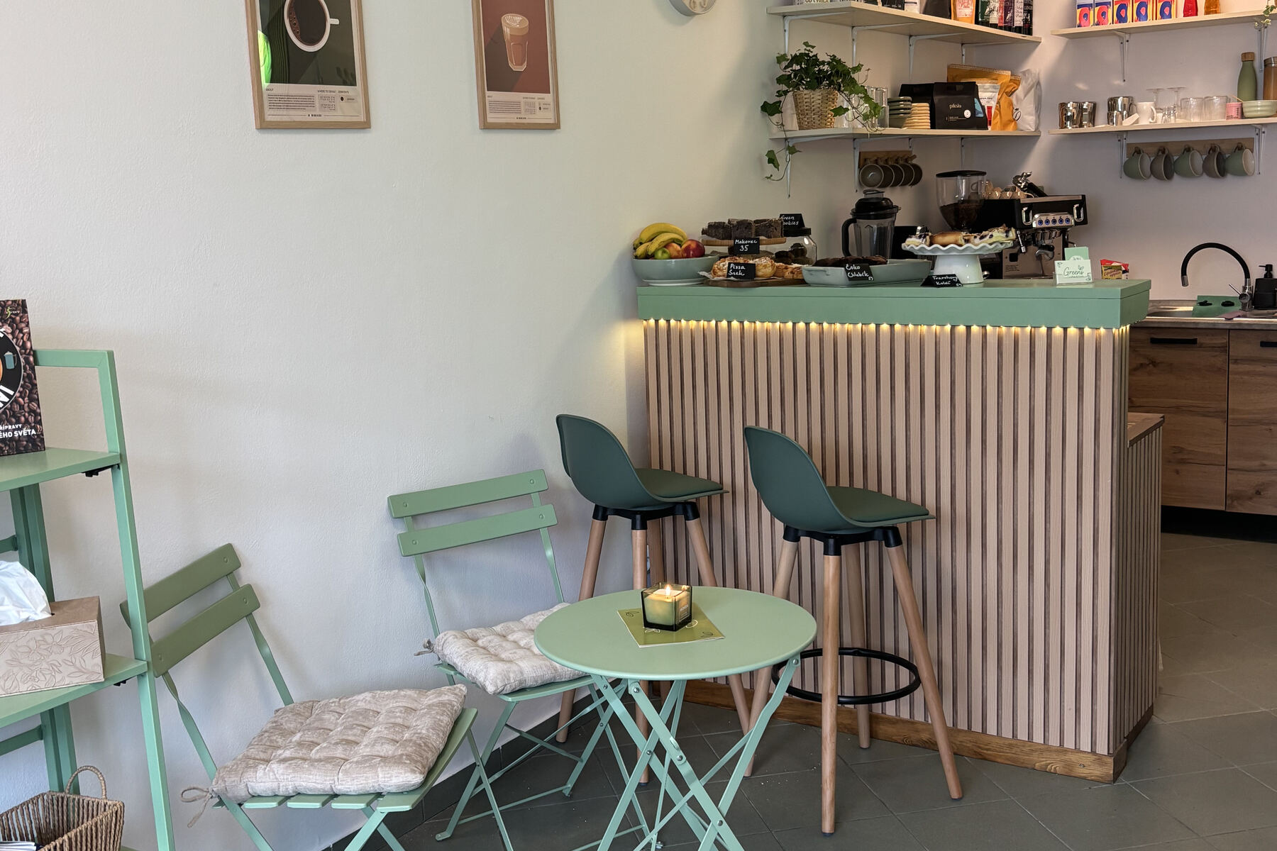 Interiér Greens — bar s vysokými židlemi a stolek se svíčkou